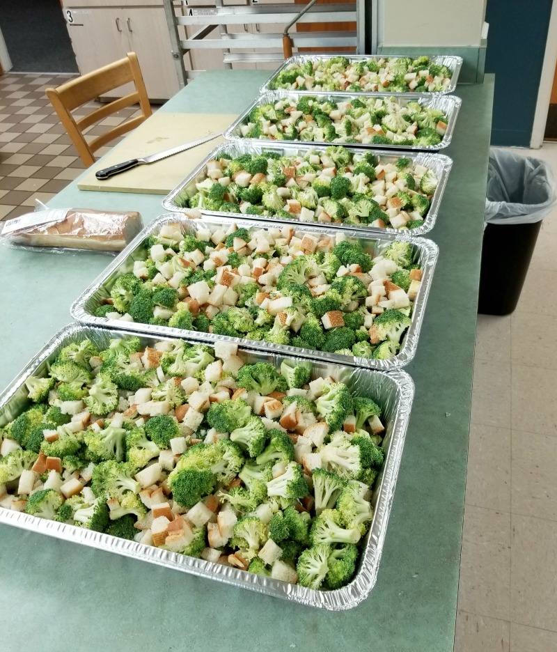 view in the kitchen with 4 pans of broccoli and bread