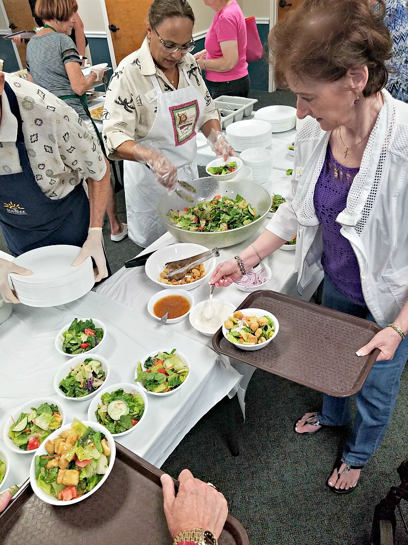 women and volunteers around a table getting salad