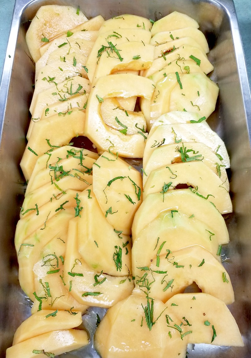 view into a hotel pan of canteloupe drizzled with honey and mint sprinkled over top. simple recipes like this make cooking for a crowd easier.