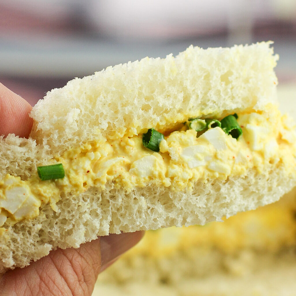 close view of hand holding sandwich to show deviled egg filling