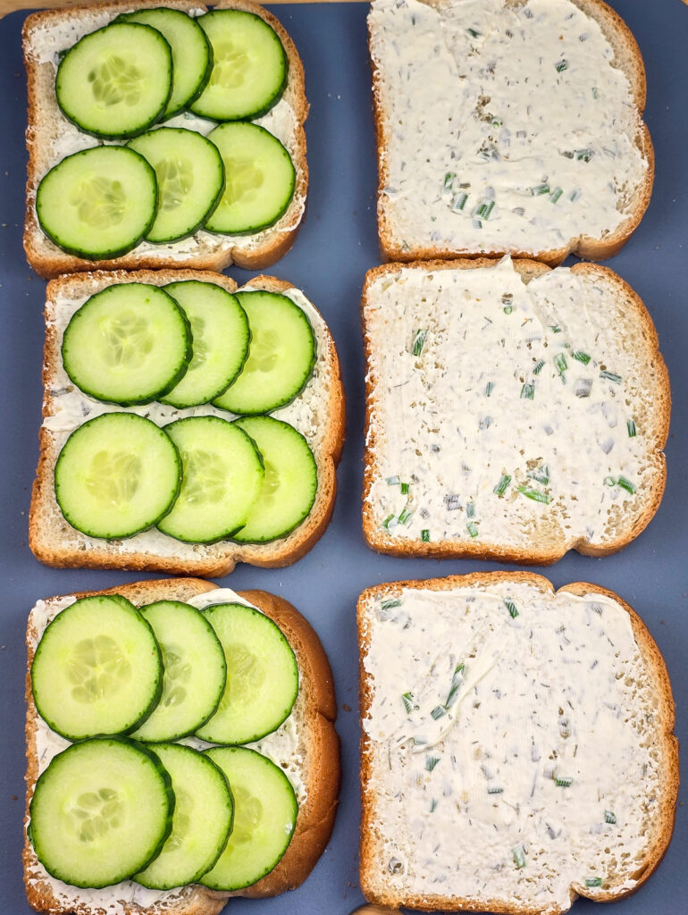 6 slices bread on board, all topped with cream cheese layer. Three slices also have cucumber layer.