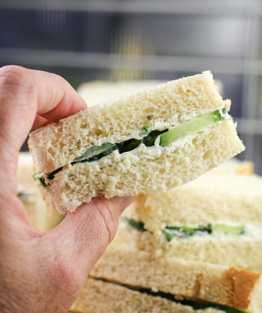 hand holding a cucumber sandwich