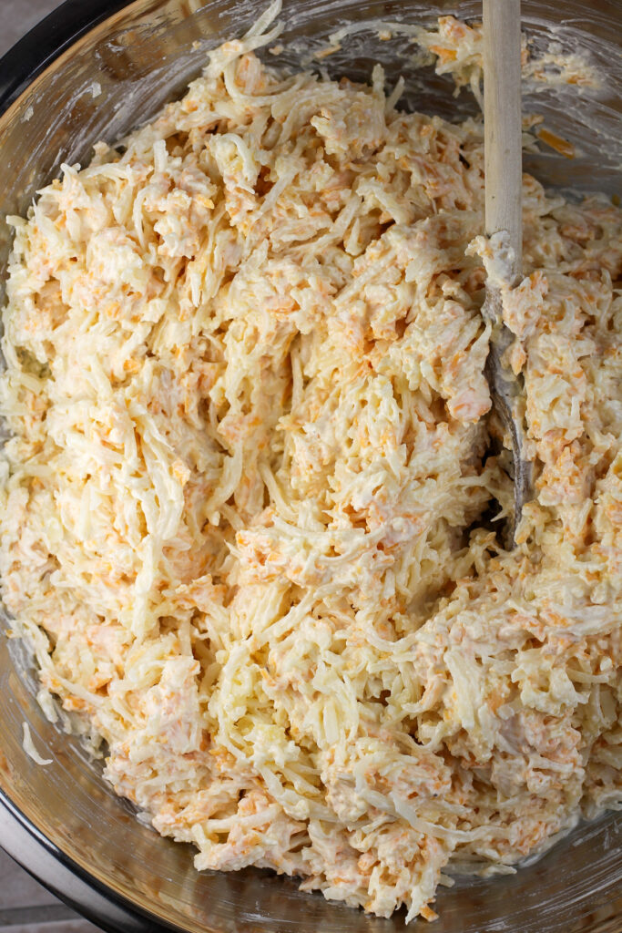 hashbrown casserole ingredients combined in large mixing bowl with wood spoon