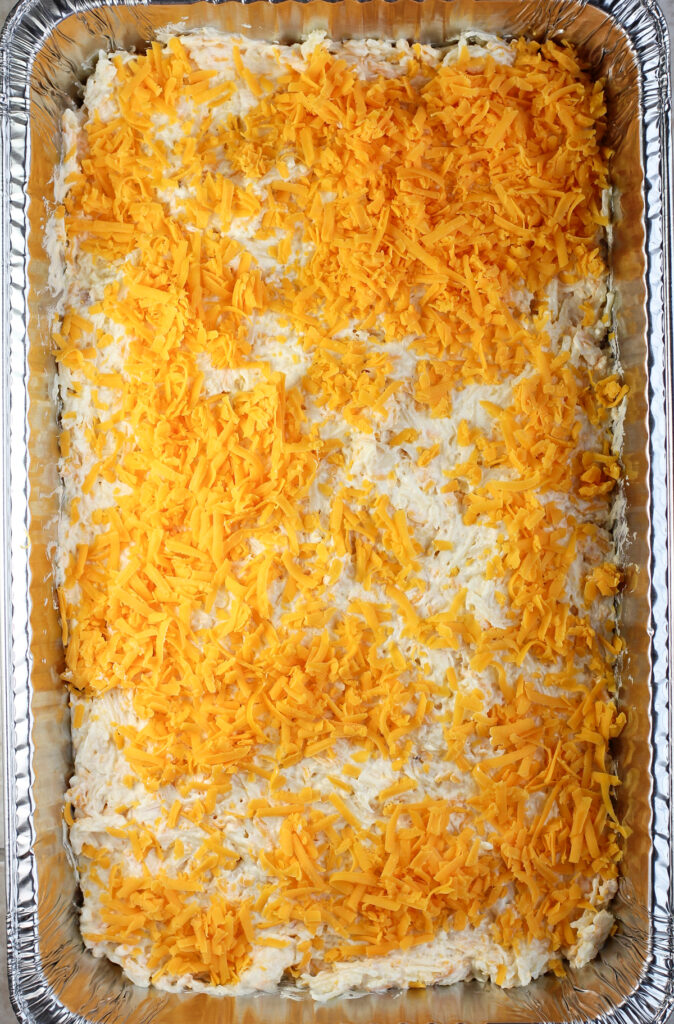 assembled hashbrown casserole in hotel pan topped with cheese before cooking