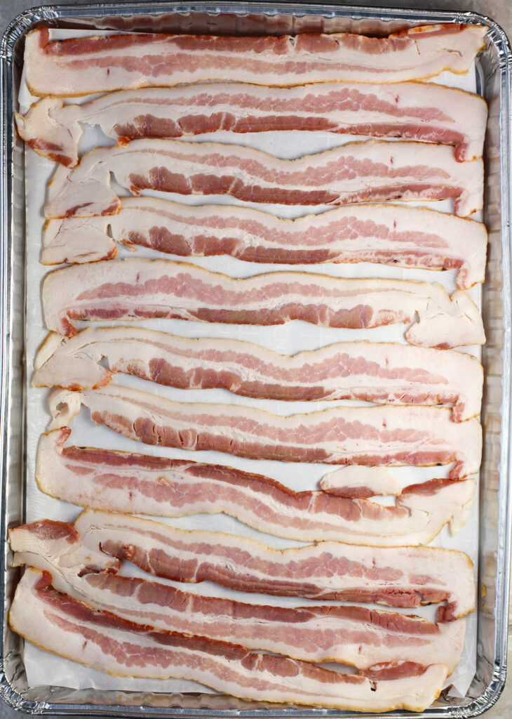 uncooked bacon in a single layer on parchment paper on bake sheet