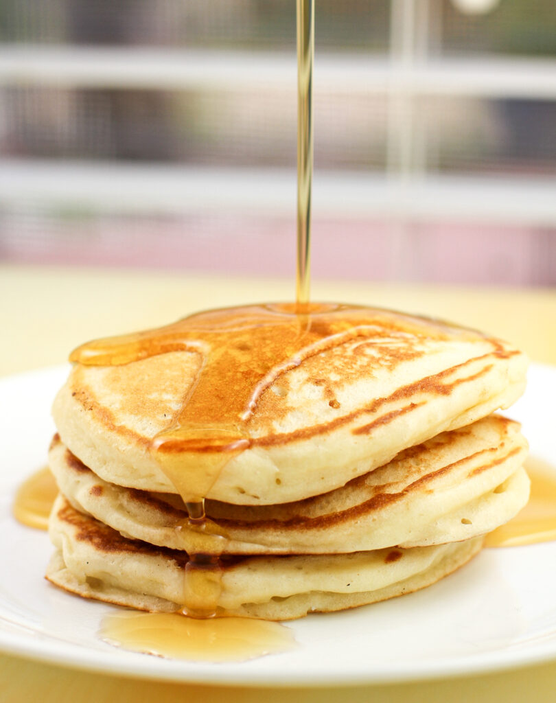3 pancakes on white dish with syrup being poured overtop