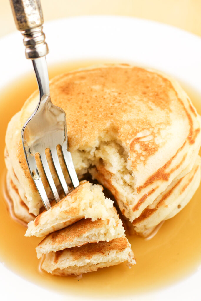fork holding bite of buttermilk pancakes. three pancakes are stacked by the fork with syrup