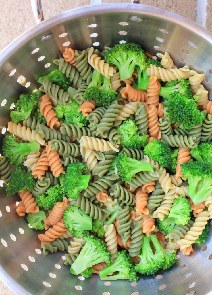 cooked tri-color rotini pasta and broccoli in colander