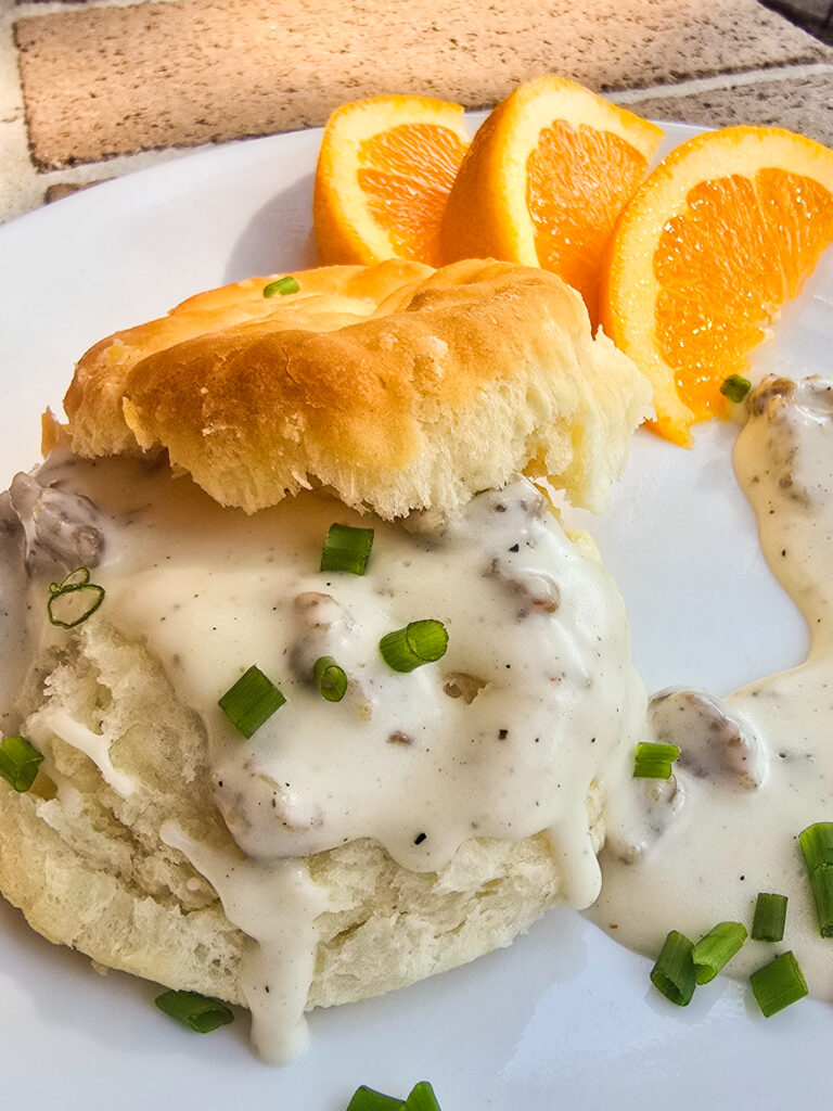 split biscuit on white plate with sausage gravy; sliced orange in the background