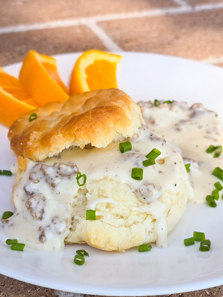 split biscuit on white plate with sausage gravy; sliced orange in the background