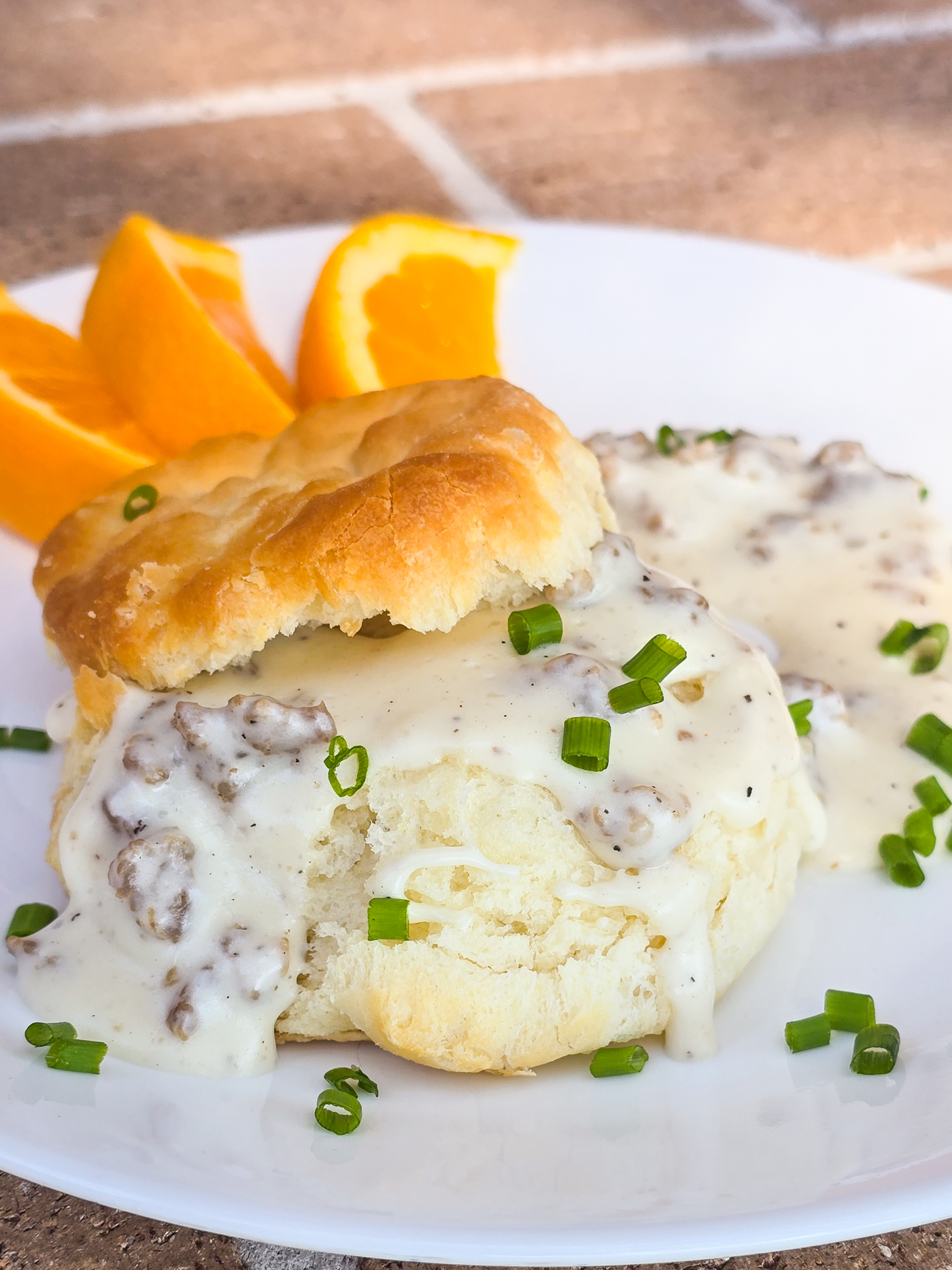 split biscuit on white plate with sausage gravy; sliced orange in the background