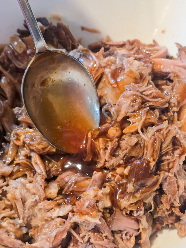spoon putting marinade on shredded pork