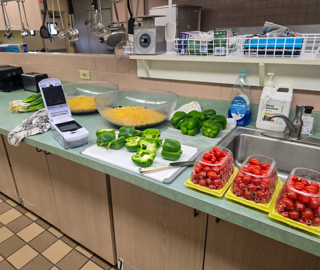 bell peppers beside chopper on counter with large bowls of black beans and corn. there are also grape tomatoes in containers