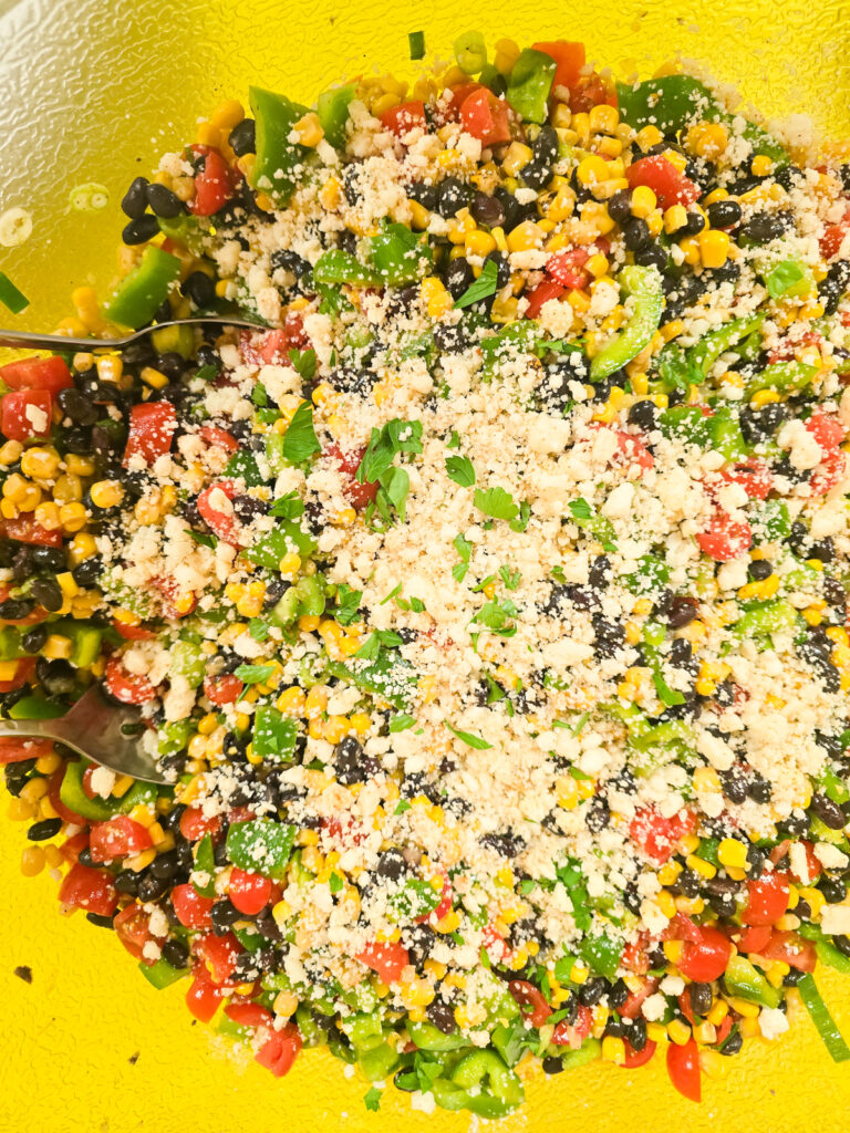 close top down view into large bowl with prepared black bean and corn salad topped with cheese