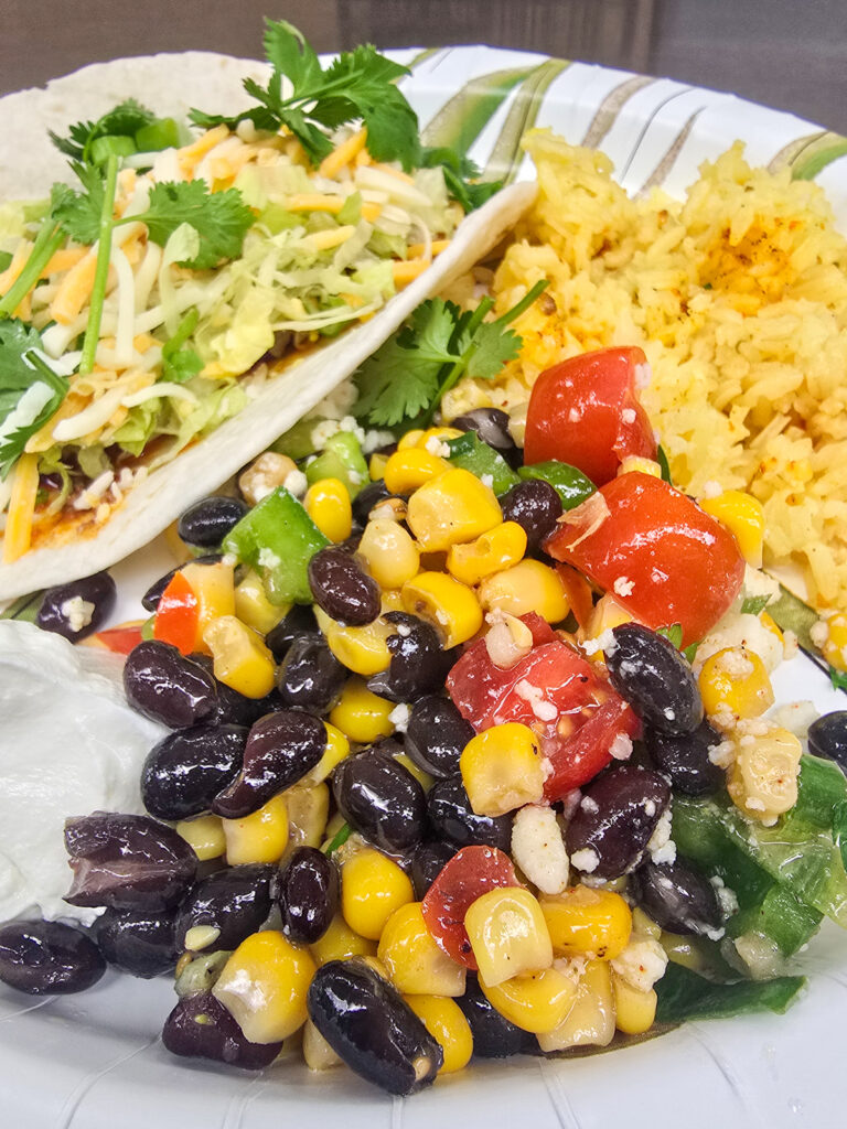 serving of black bean and corn salad on plate with a taco and yellow rice