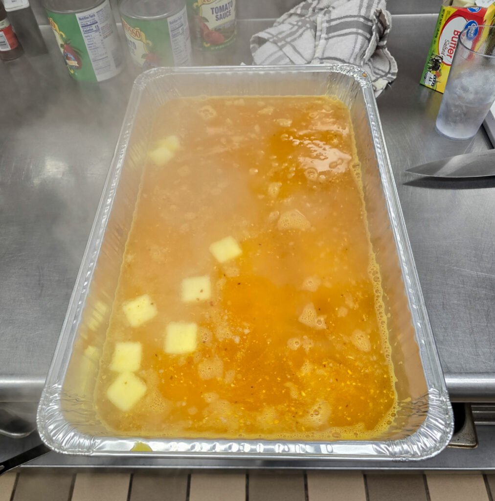 Pouring measured boiling water into large commercial hotel pans filled with dry yellow rice before baking