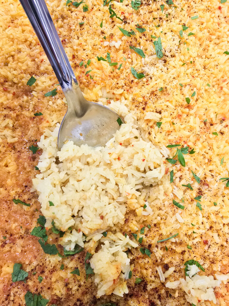 Fluffy, bright yellow cooked rice being scooped out of a large commercial catering pan with a metal serving spoon.