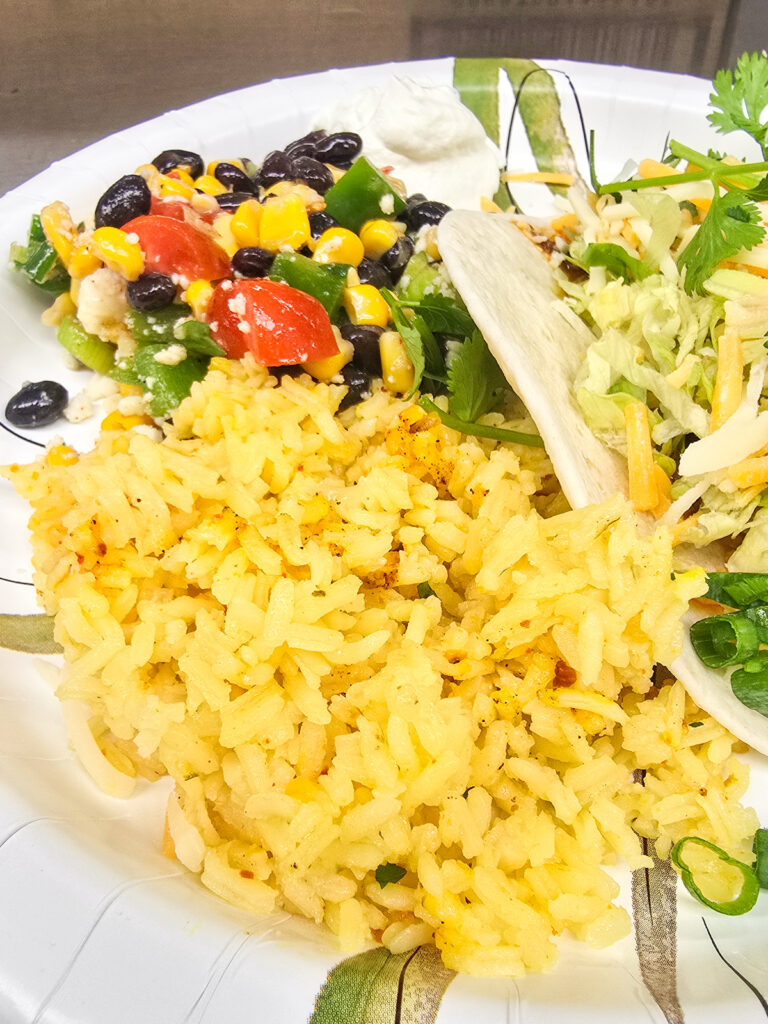 A plated serving of oven-baked yellow rice next to a colorful salad and main dish for a large crowd meal