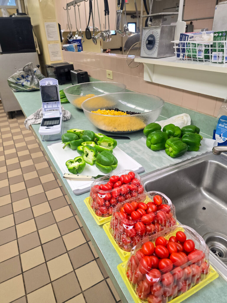 counter view showing salad ingredients corn, tomatoes, and green bell peppers being chopped