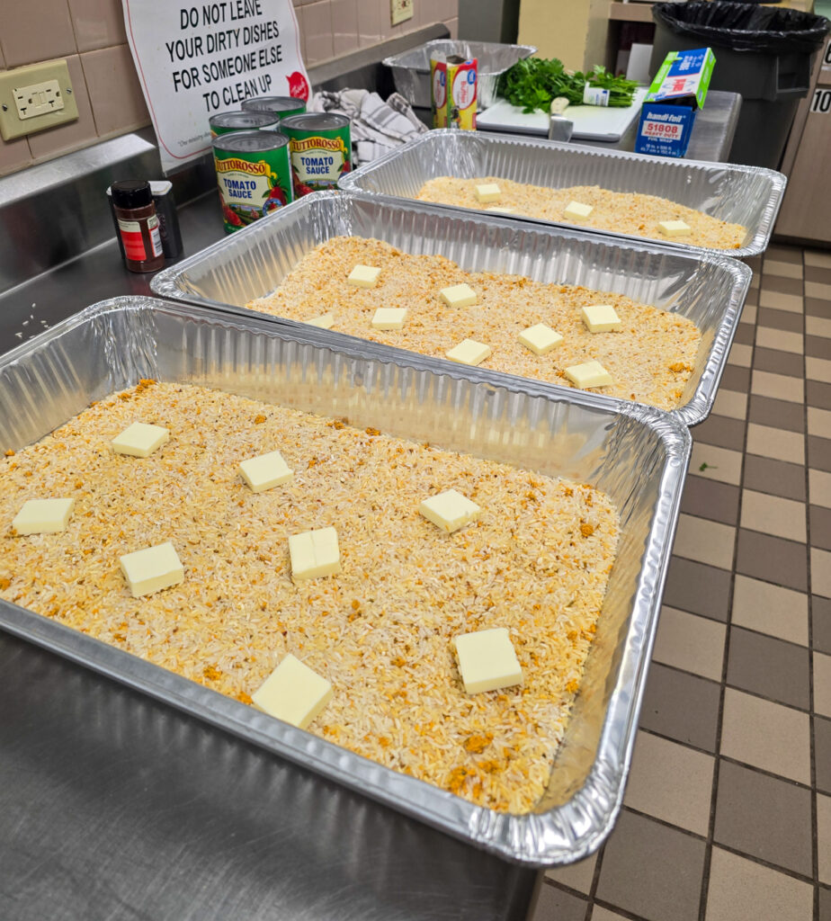 3 hotel pans with uncooked yellow rice topped with tablespoon pieces of butter