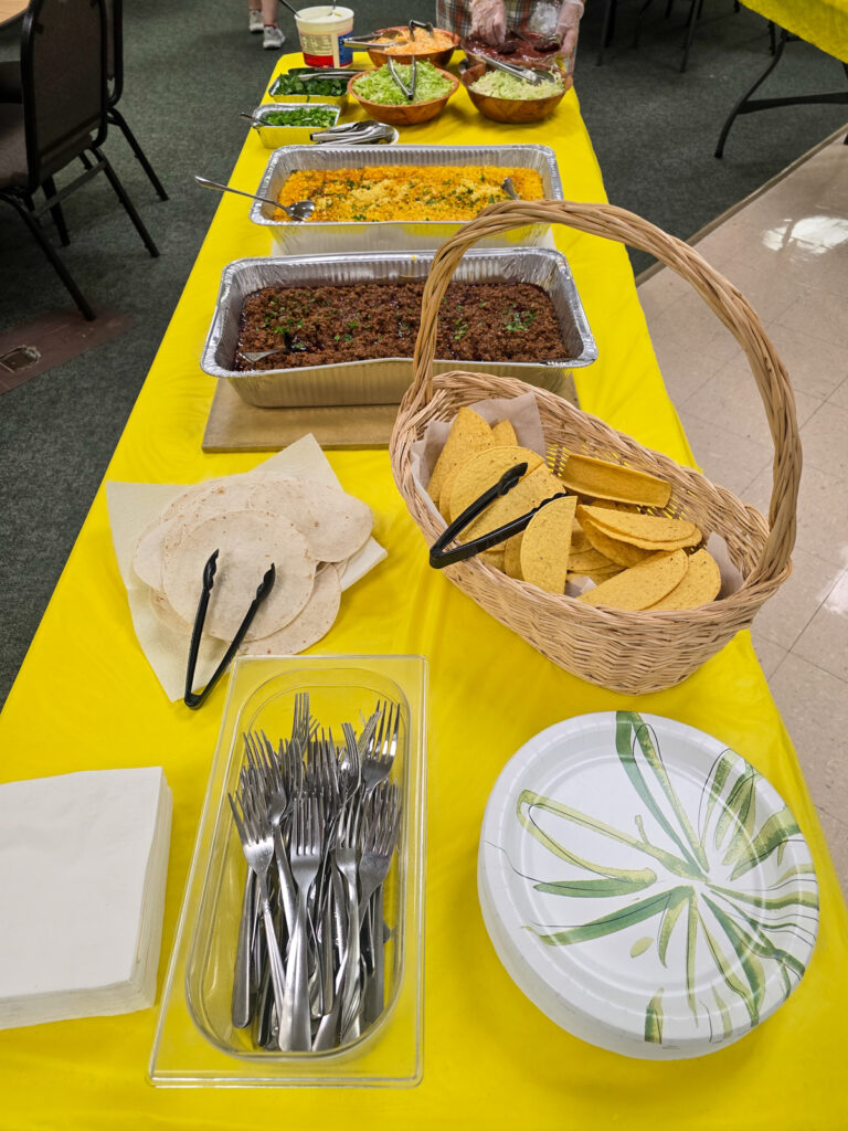 paper plates, silverware, napkins, tortillas, and tongs on yellow tablecloth
