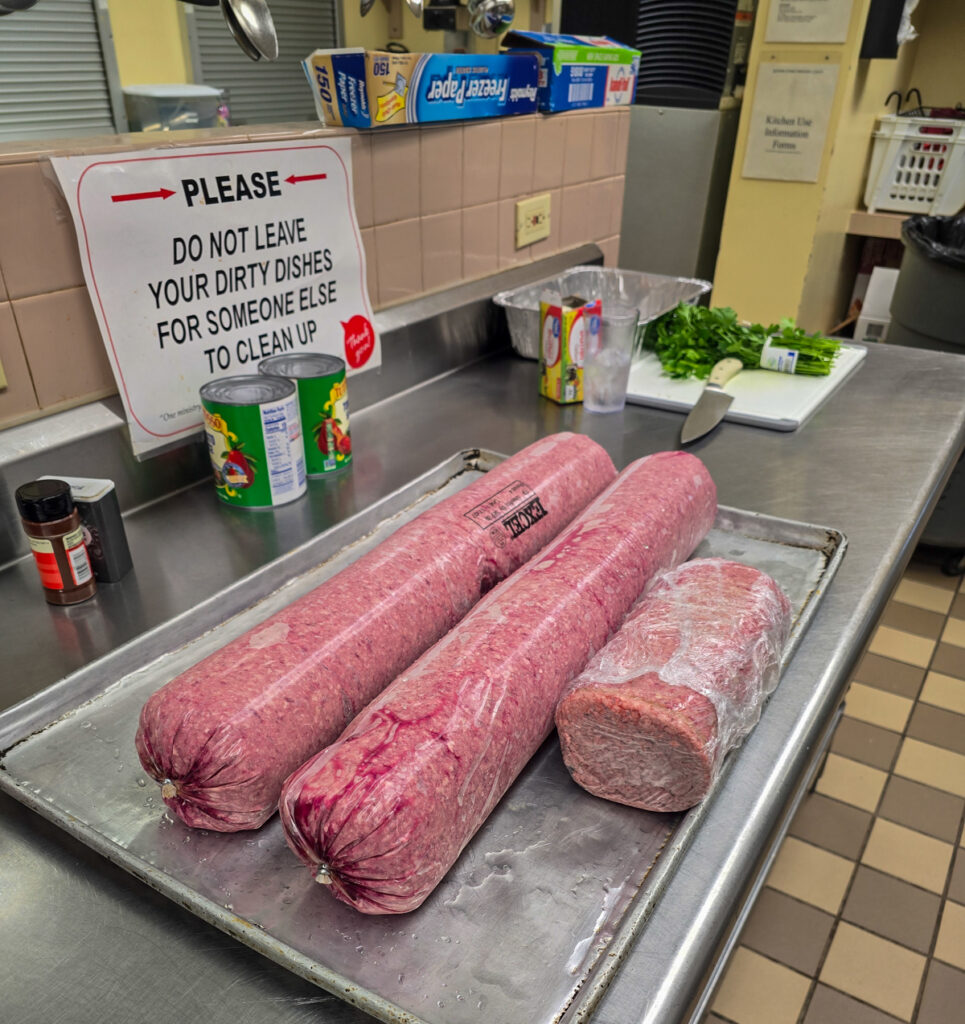 Two long rolls and a smaller block of plastic-wrapped raw ground beef on a baking tray on a kitchen counter