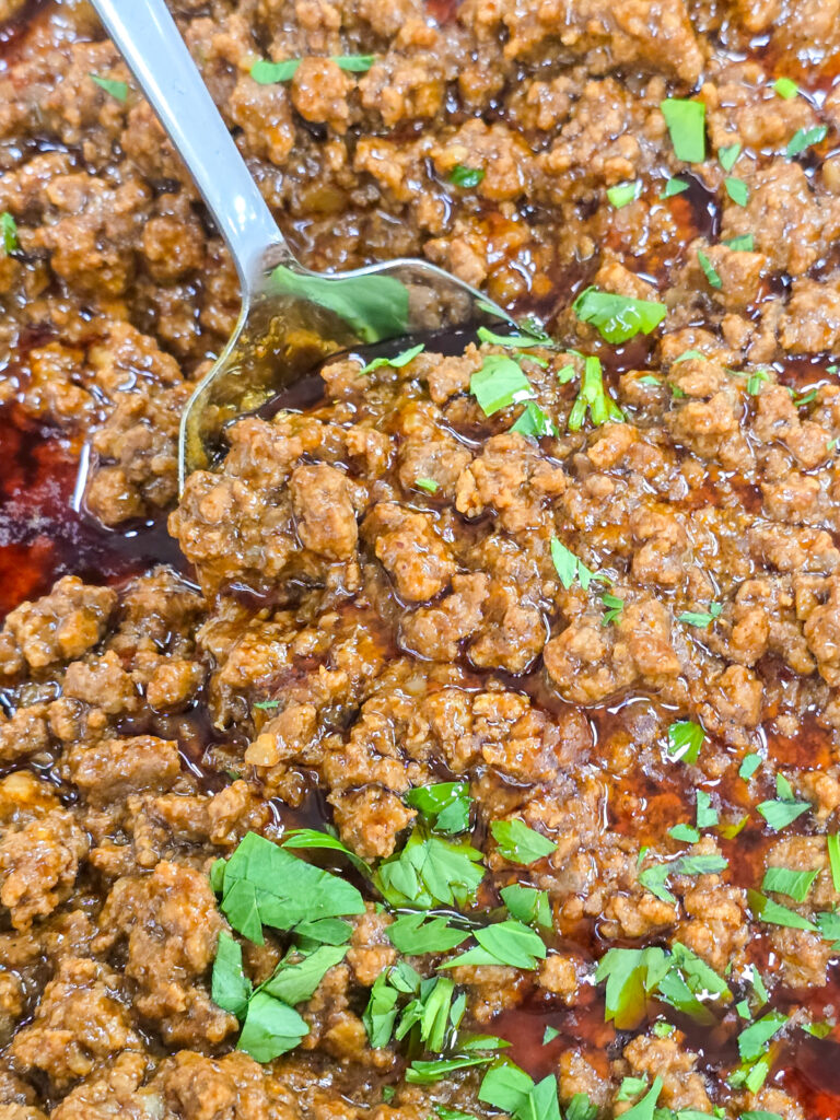 Seasoned ground taco meat garnished with fresh chopped herbs, being scooped with a metal spoon
